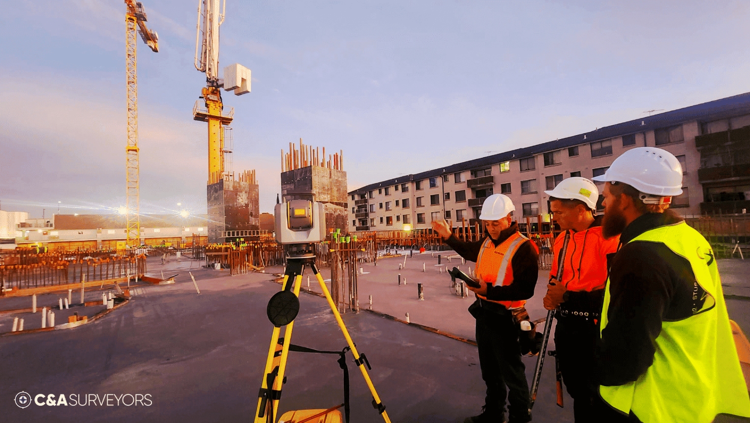 Three Men Using Surveying Tools On A Work Site